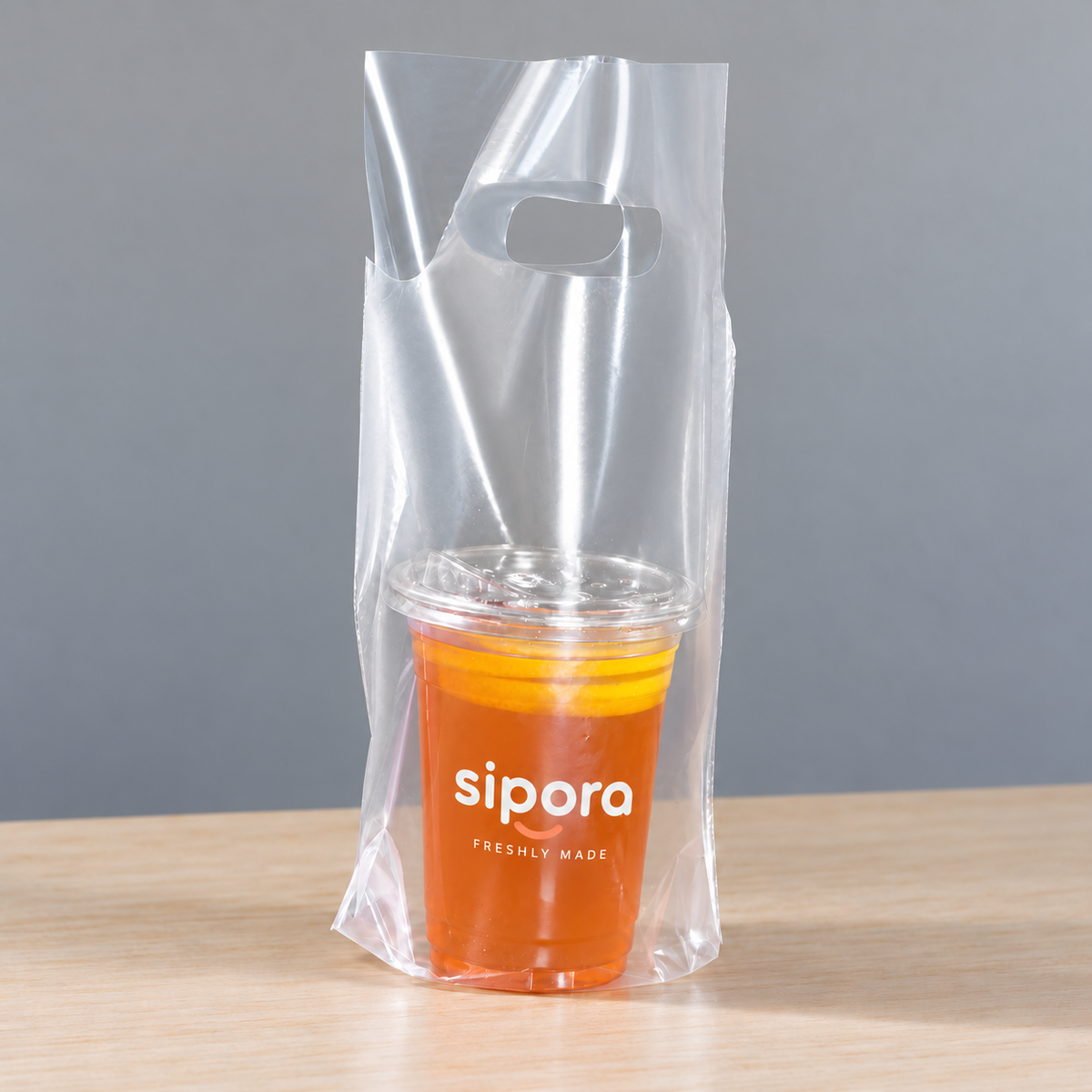 Clear PE single-cup takeaway bag with die-cut handle holding a lidded orange lemon tea.