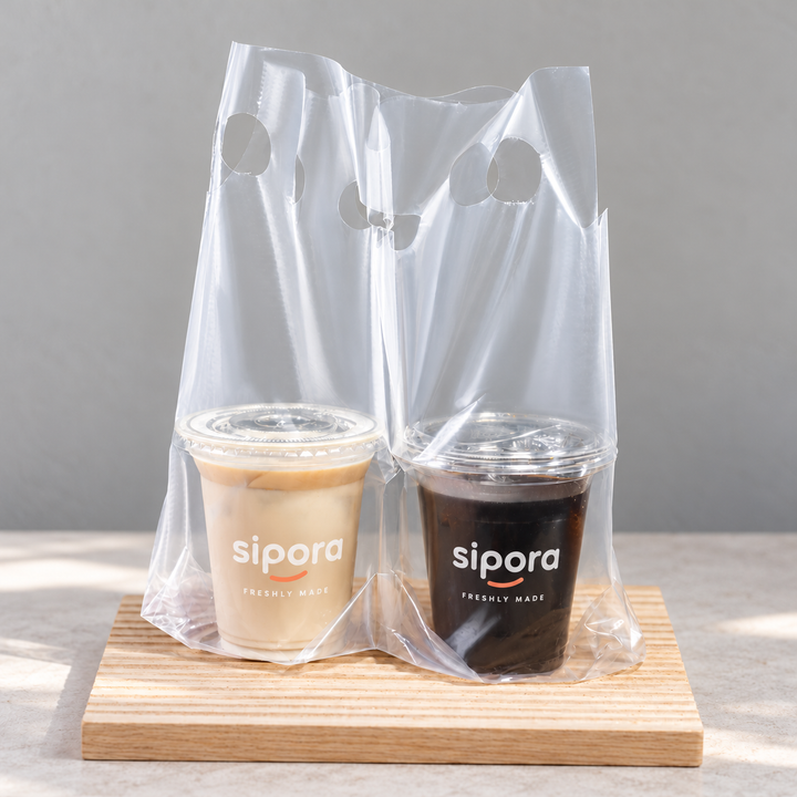 Clear PE two-cup takeaway carrier bag holding a milk tea and a dark coffee side by side.