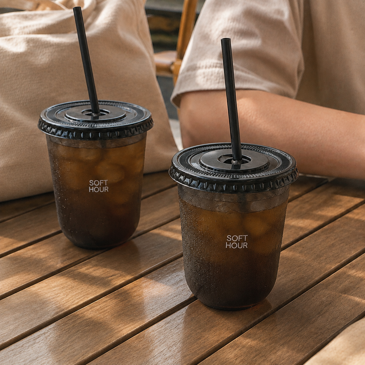 Two custom black PET U-shaped cold cups with straw-slot lids and black straws, served with iced coffee at a cafe table.